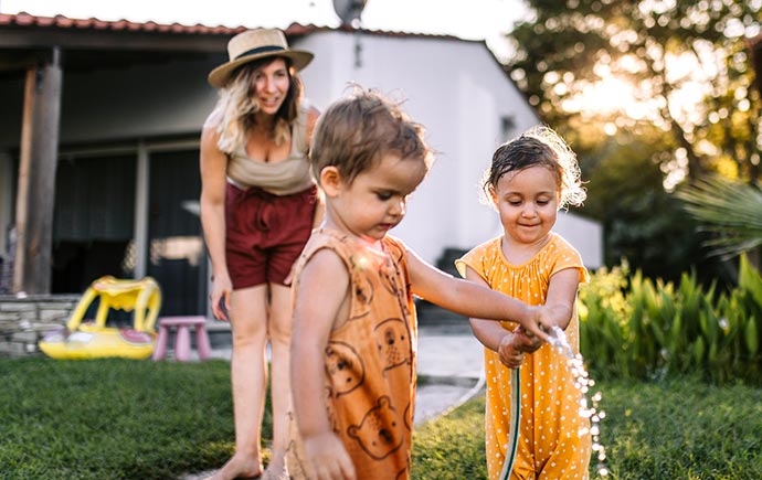 Mom and two children that are playing with the hose in their backyard.