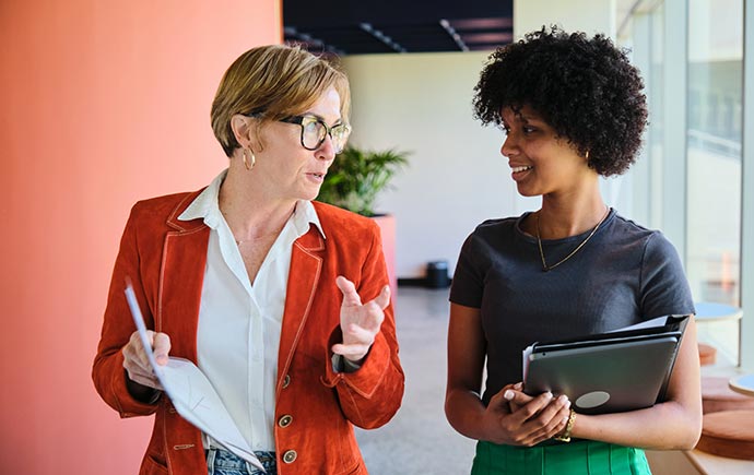 Two coworkers walking and talking in the office hallway.